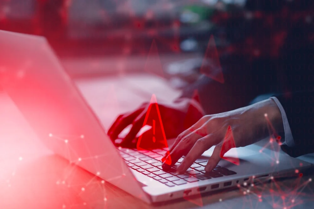 Hands typing on a laptop with digital warning alerts, symbolizing KYC fraud detection and early-stage identity risk signals