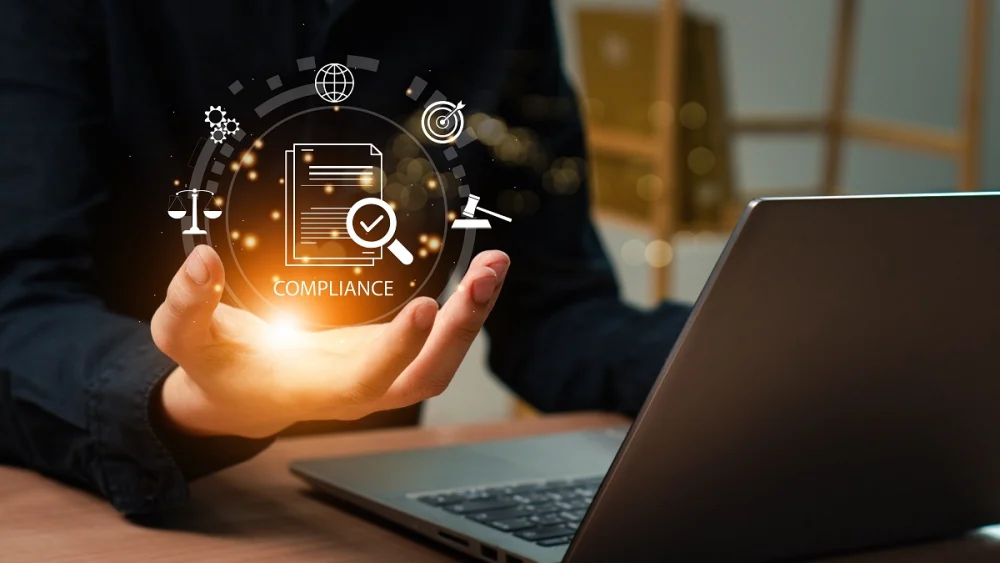 Individual holding a glowing virtual compliance icon with surrounding symbols for legal balance, contracts, and performance metrics